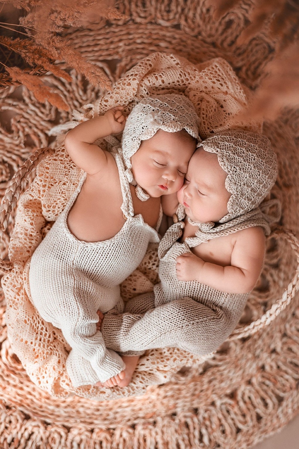 Zwei schlafende Babys in cremefarbenen Strickmützen auf einer gehäkelten Decke