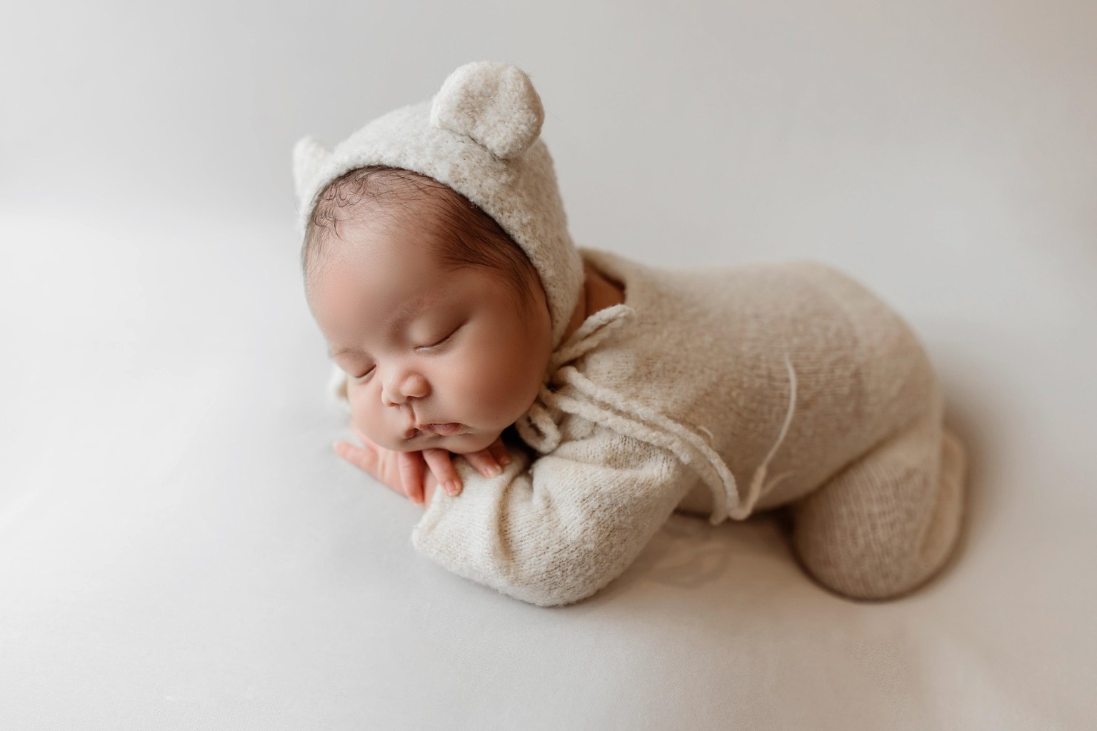 Schlafendes Baby in beigem Strickoutfit mit Mütze auf hellem Hintergrund