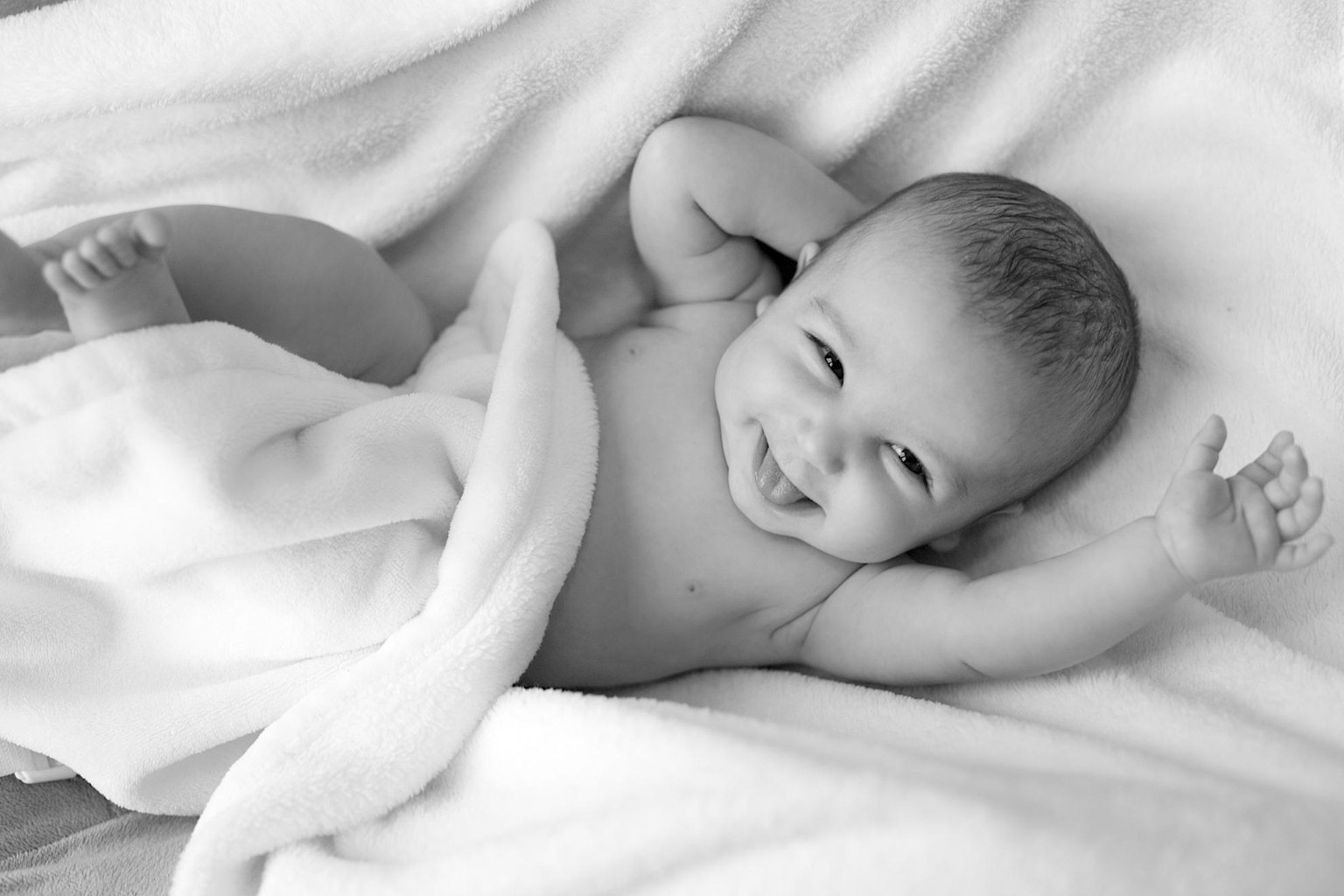 Lächelndes Baby unter einer weißen Decke in Schwarz-Weiß